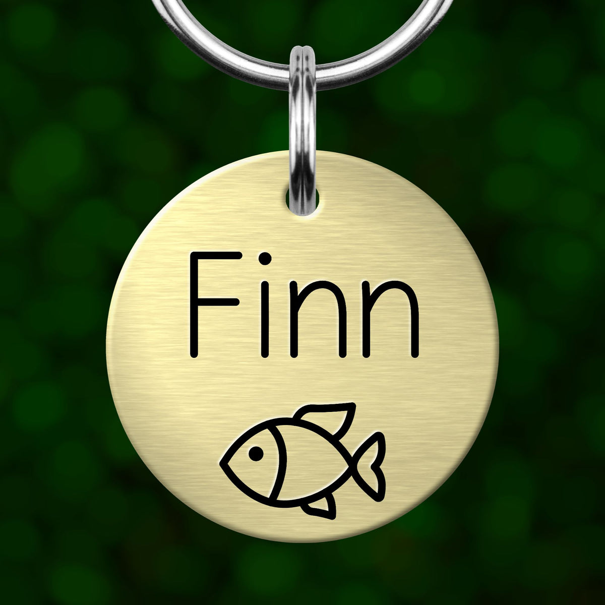 A round metal name tag with the name "Finn" written on it, featuring a simple black fish illustration.