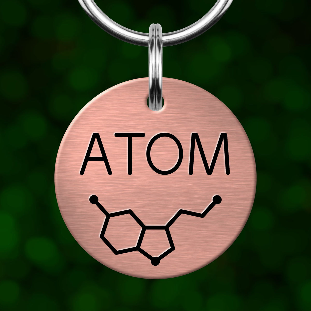 A round metal tag with the word "ATOM" printed on it, along with a chemical symbol for an atom.