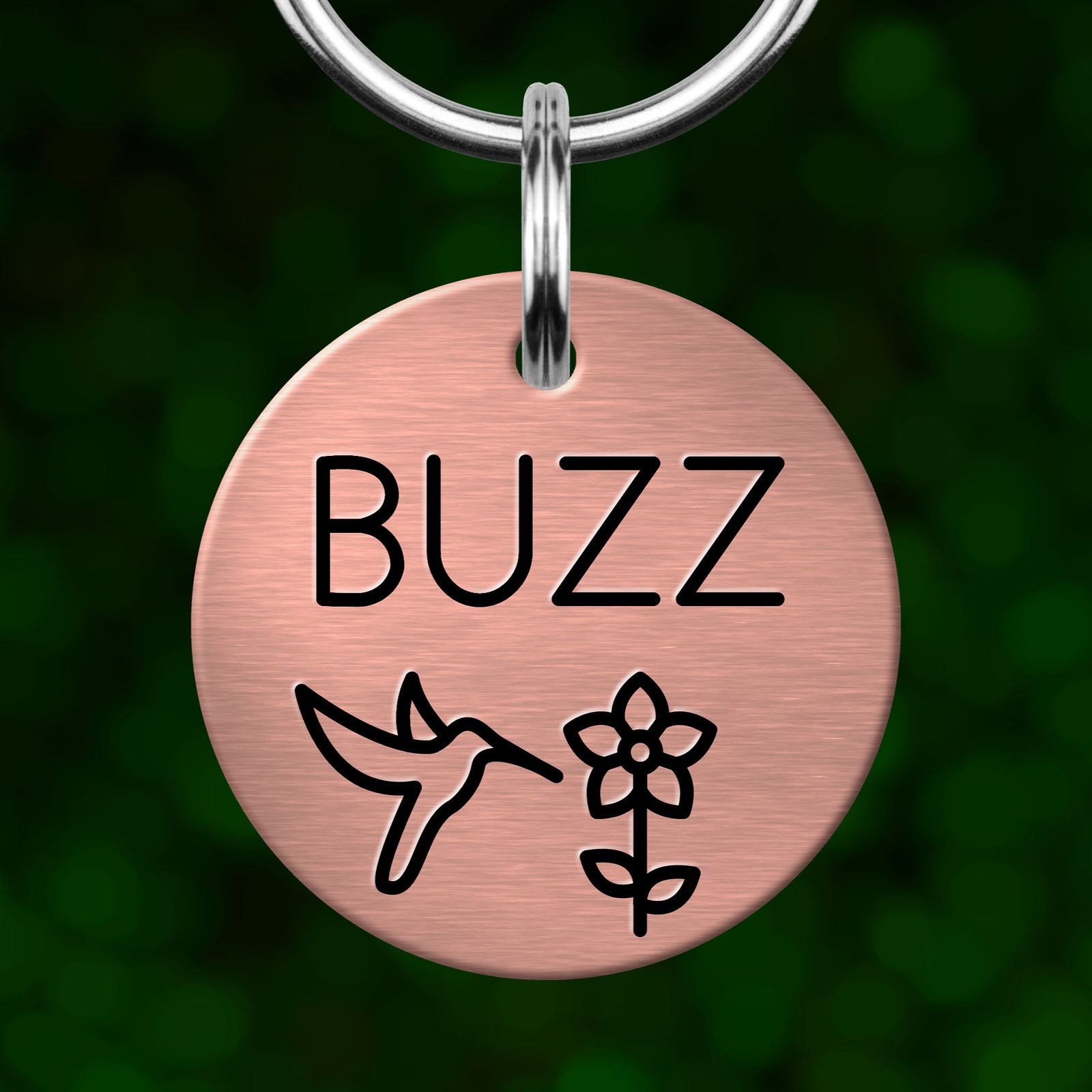 A round metal pet tag with the word "BUZZ" printed on it, featuring a bird and a flower design.