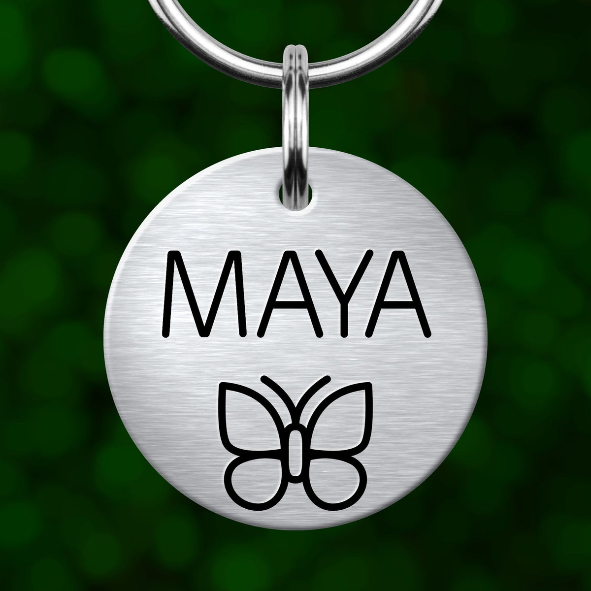 A silver metal name tag with the name "MAYA" printed on it, along with a simple black butterfly graphic.
