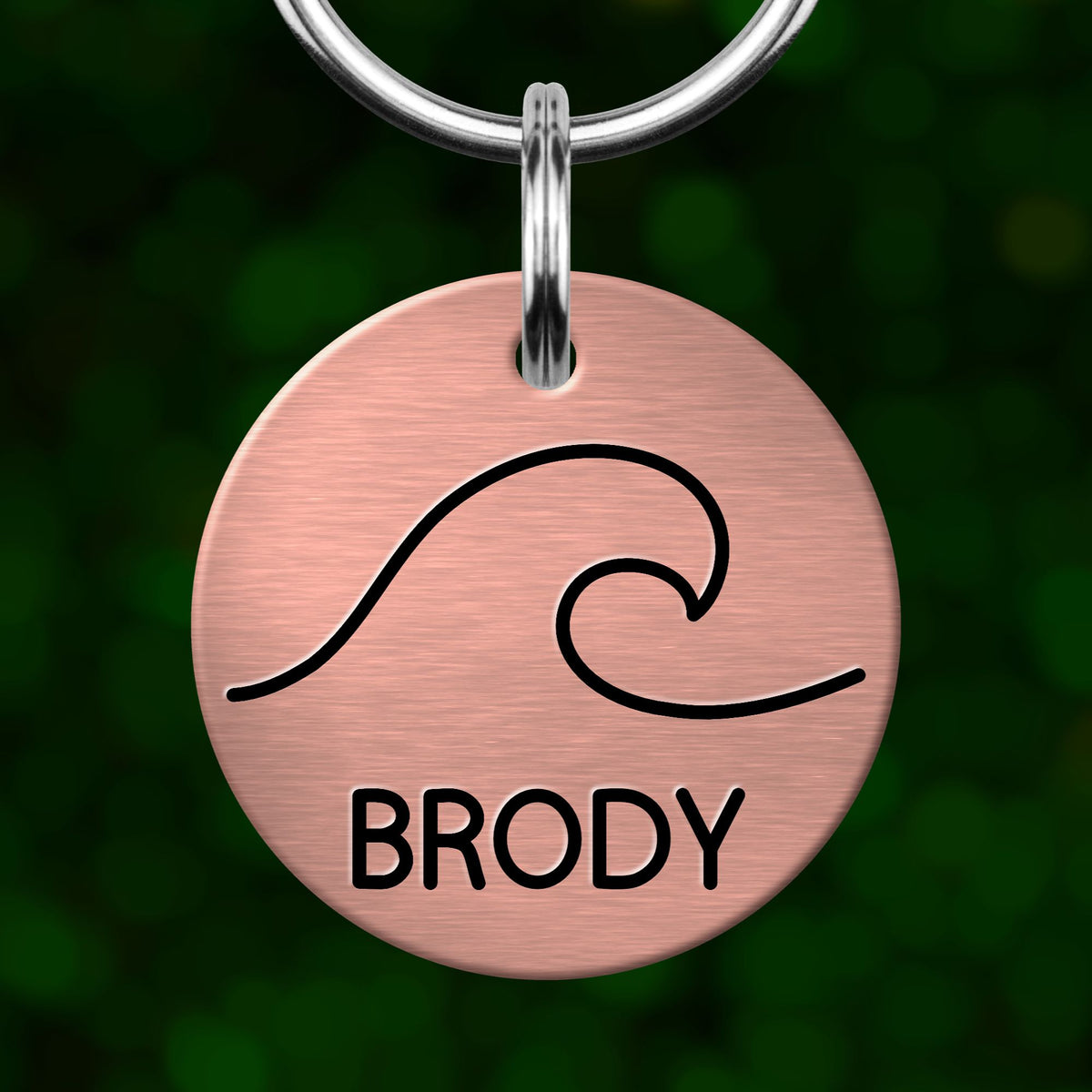 A round metal pet tag with a wave design and the word "BRODY" printed on it.