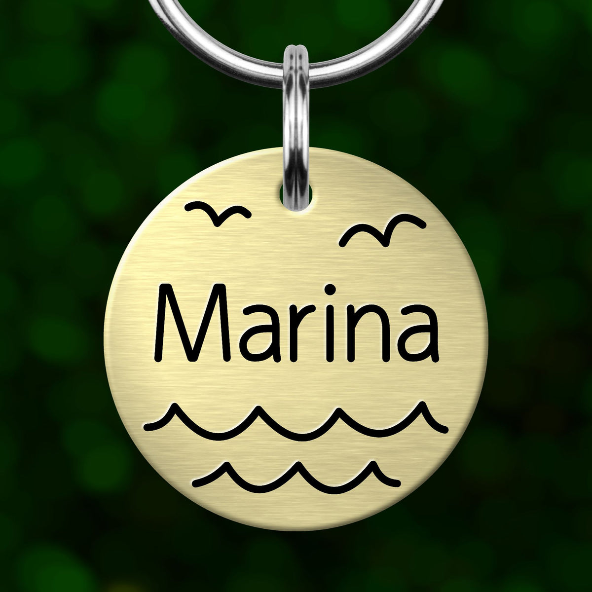 A round metal pet tag with the name "Marina" written on it, featuring a wave and bird design.