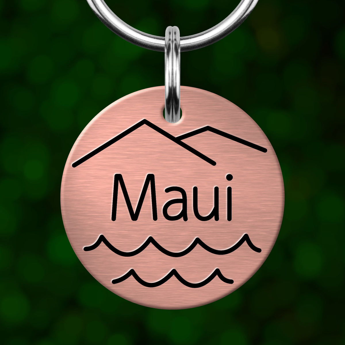 A round metal keychain with a mountain and wave design, and the word "Maui" written on it.