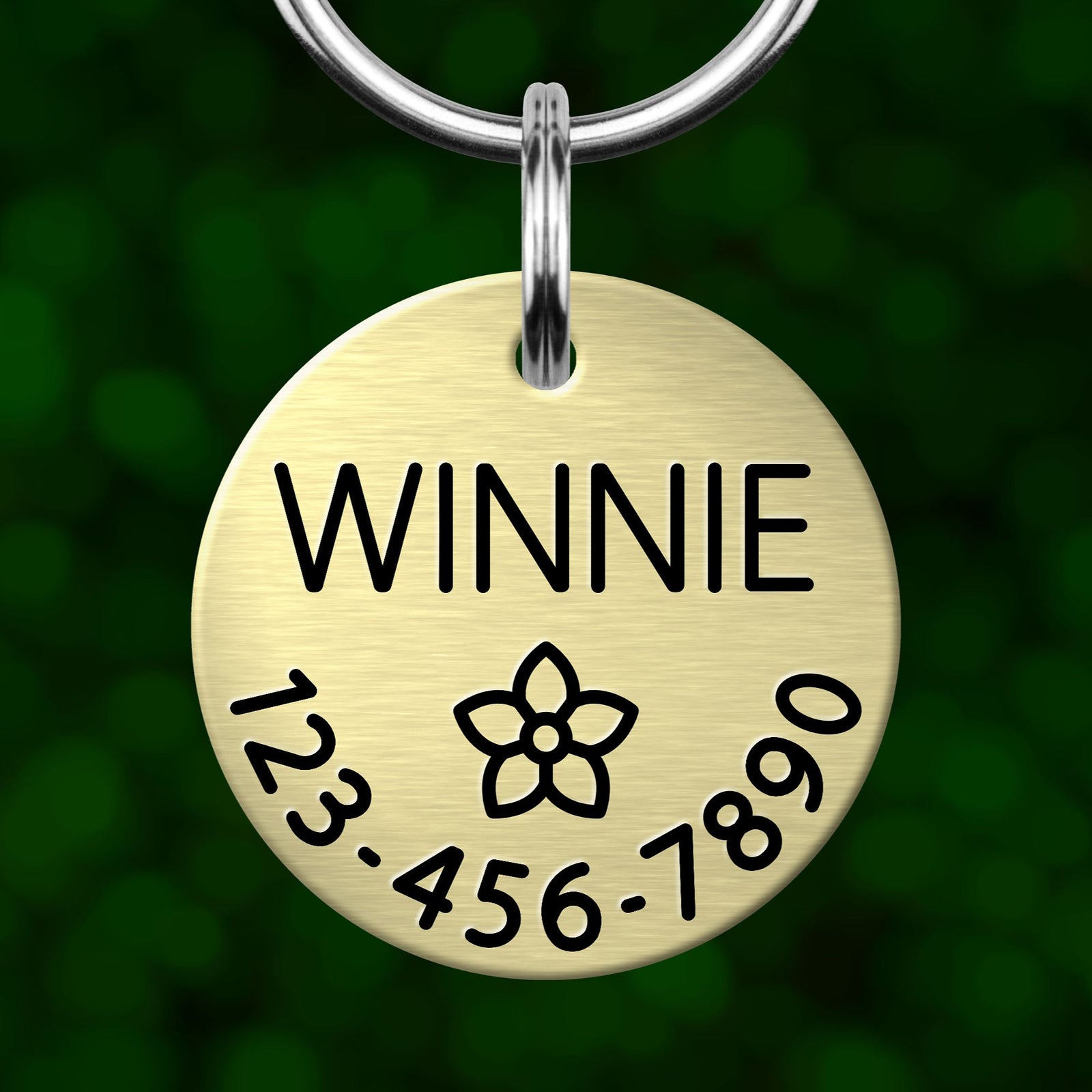 A round metal pet tag with the name "WINNIE" and a flower symbol, along with the numbers "123-456-7890".