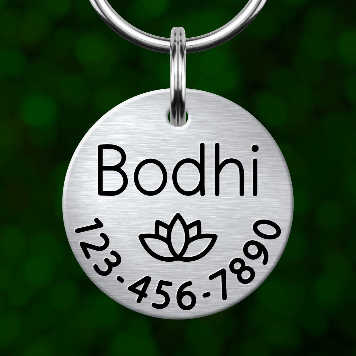 A silver-colored metal pet name tag with the name "Bodhi" and a lotus flower symbol.