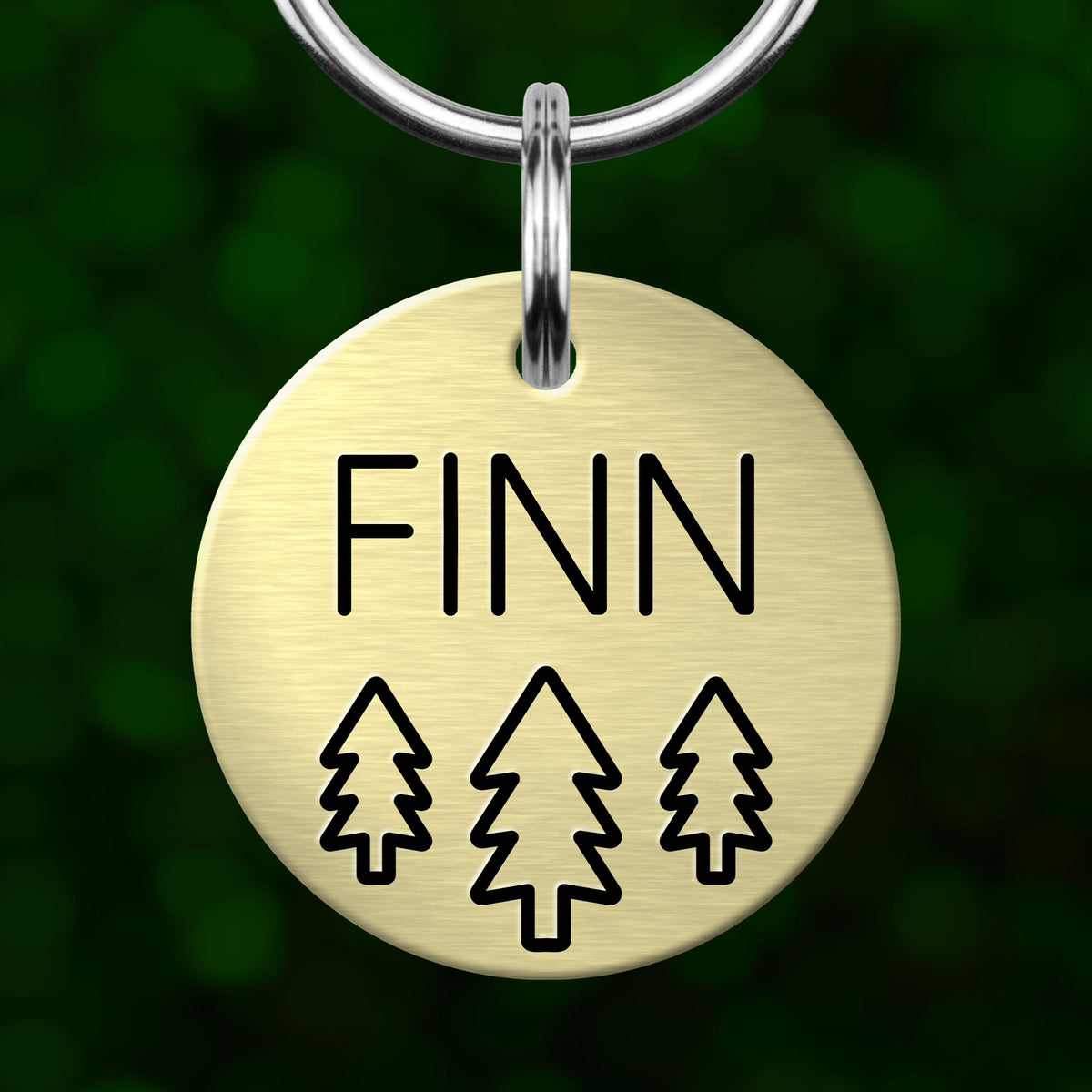 A round metal pet tag with the name "FINN" printed on it, along with three stylized tree icons.