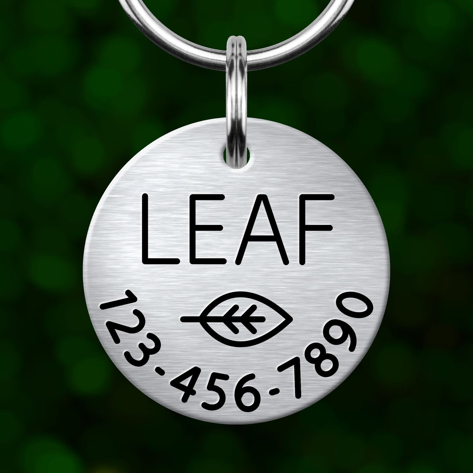 A silver circular pet tag with the word "LEAF" printed on it, along with a leaf symbol and some numbers below.