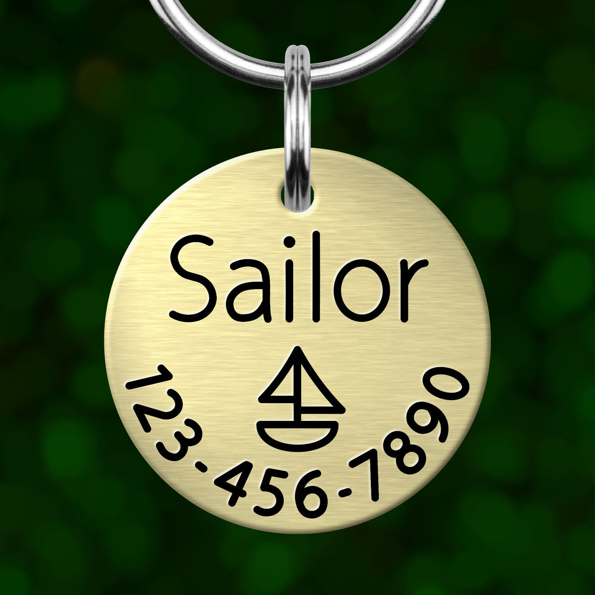 A round metal keychain tag with the name "Sailor" printed on it, along with a phone number and a symbol resembling a boat.