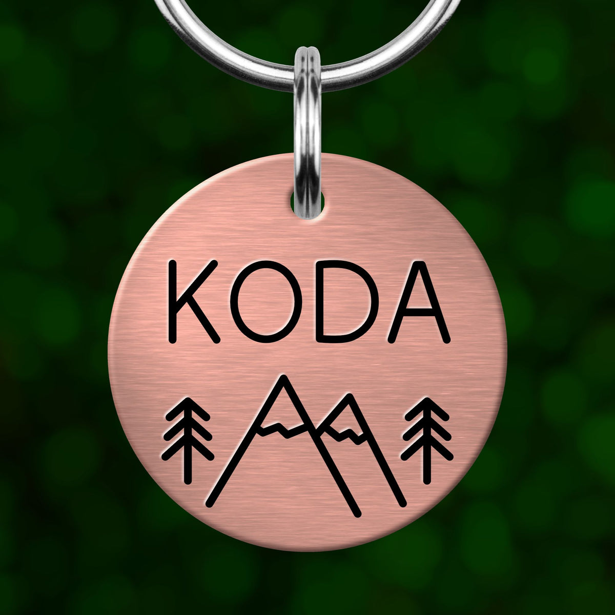 A round metal pet tag with the name 'KODA' printed on it, along with a mountain and tree symbol.
