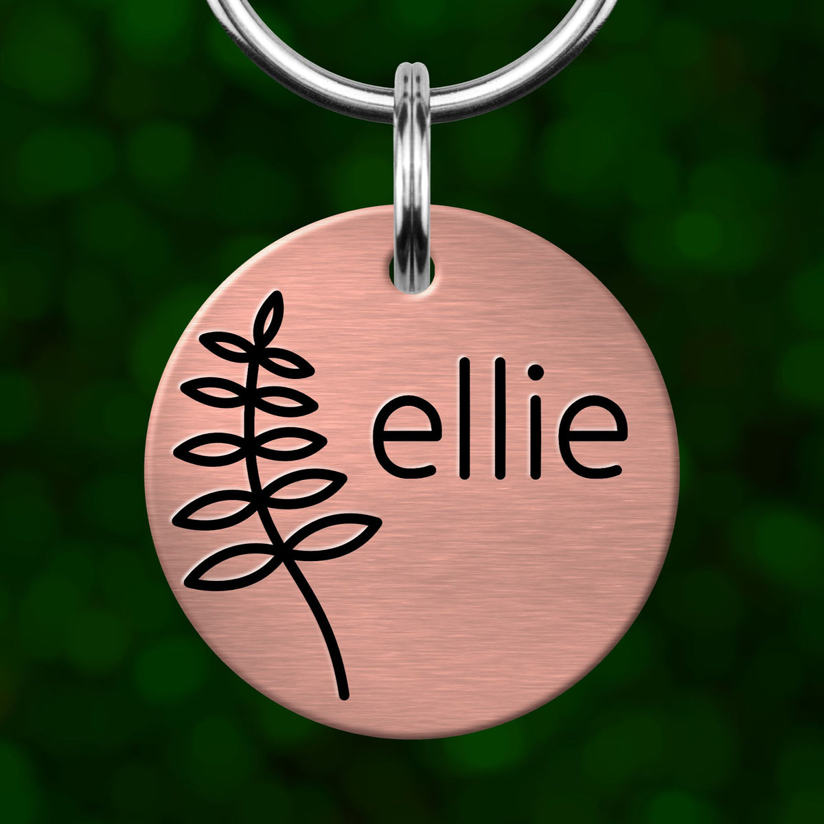 A pink circular pet tag with a black leaf design and the name "Ellie" printed on it.