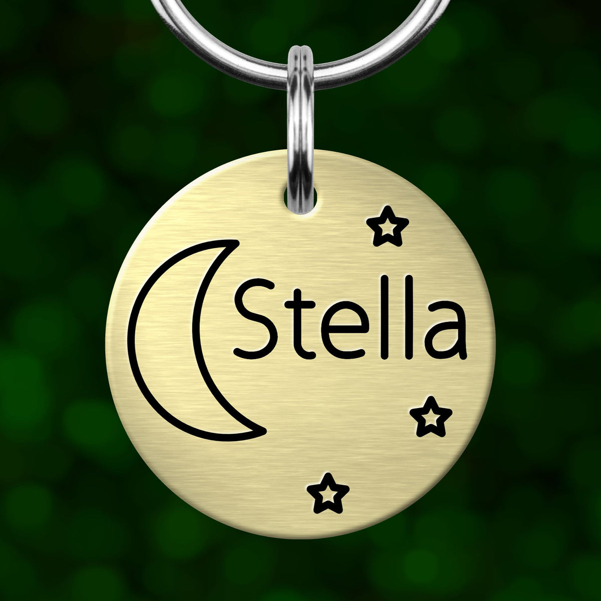 A round metal keychain tag with the name 'Stella' and stars around it, hanging from a metal hook.