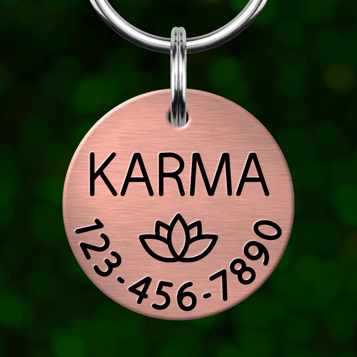 A copper-colored pet name tag with the word "KARMA" printed on it, along with a lotus flower symbol and a phone number.