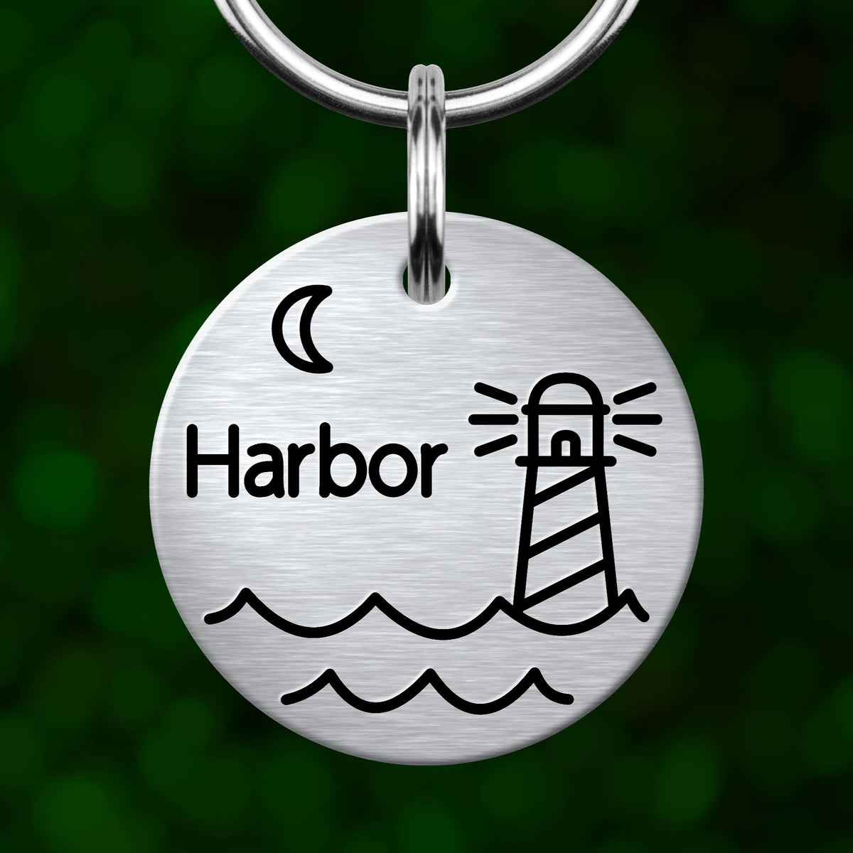 A round metal keychain with a lighthouse and waves, with the word "Harbor" written on it.
