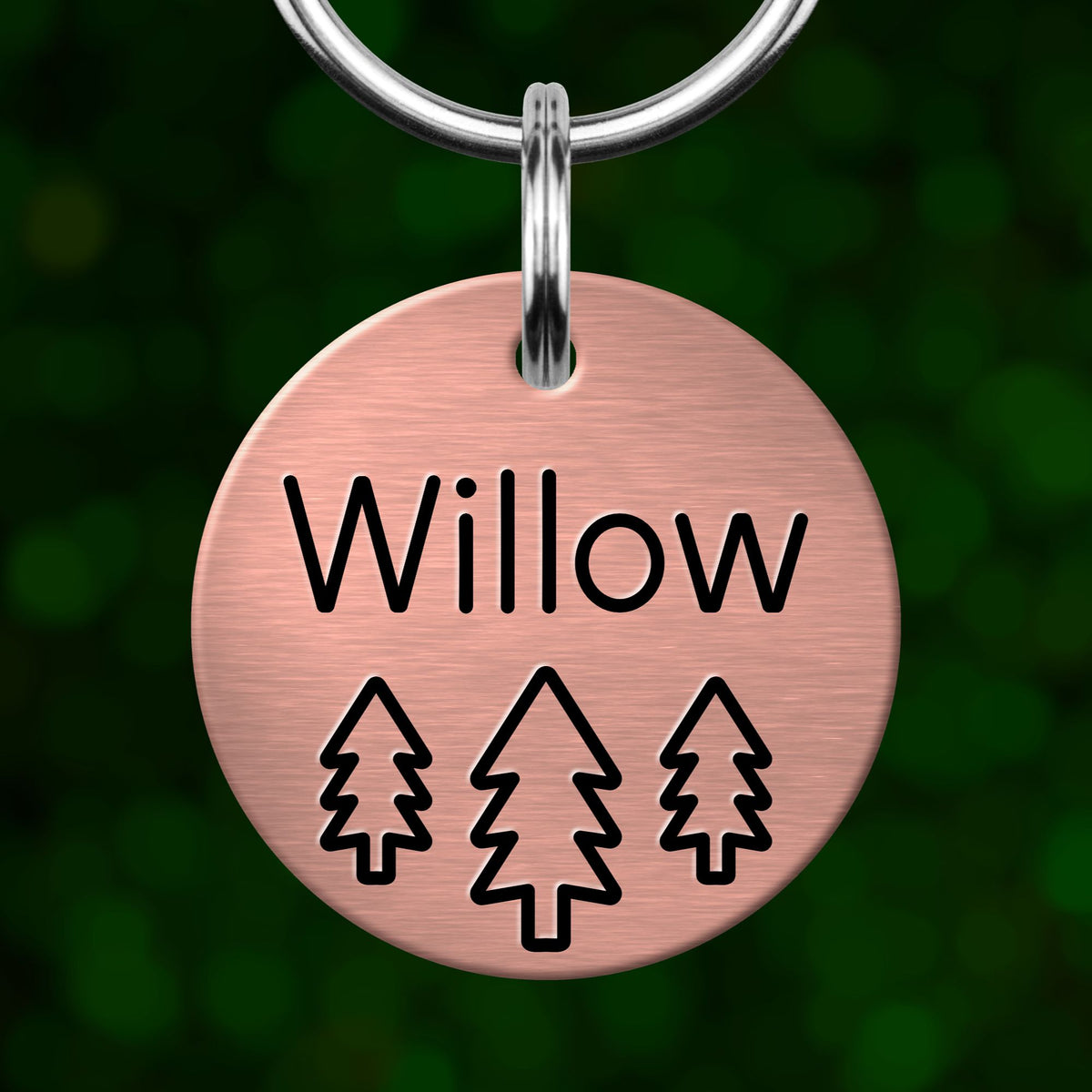 A round metal pet tag with the name "Willow" and three tree icons printed on it.