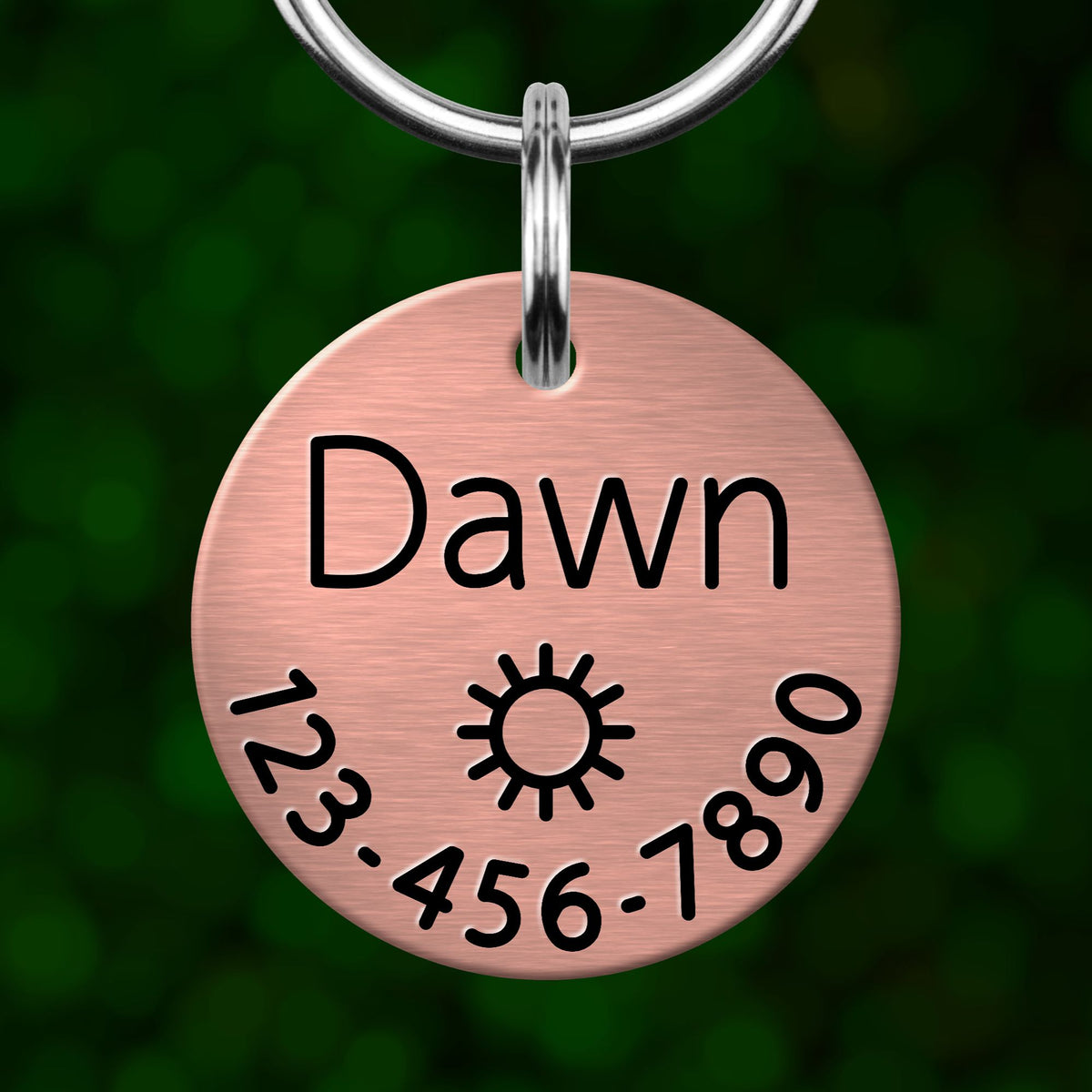 A copper-colored pet name tag with the name "Dawn" and a phone number "123-456-7890" printed on it.