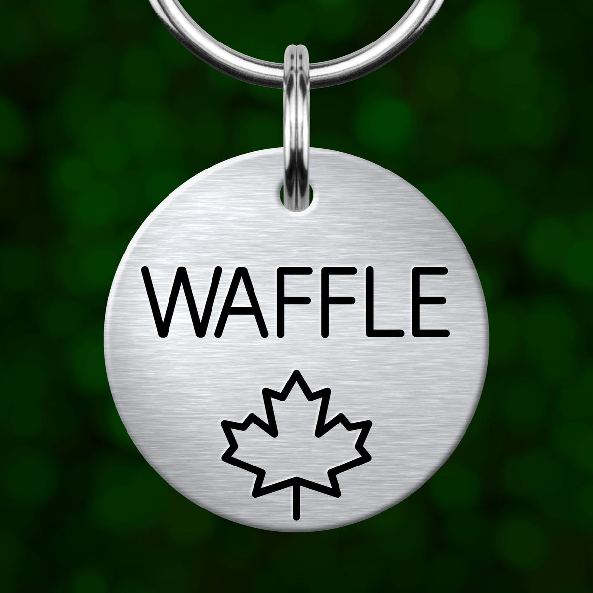 A silver-colored metal keychain with the word "Waffle" printed on it, along with a simple black maple leaf symbol.