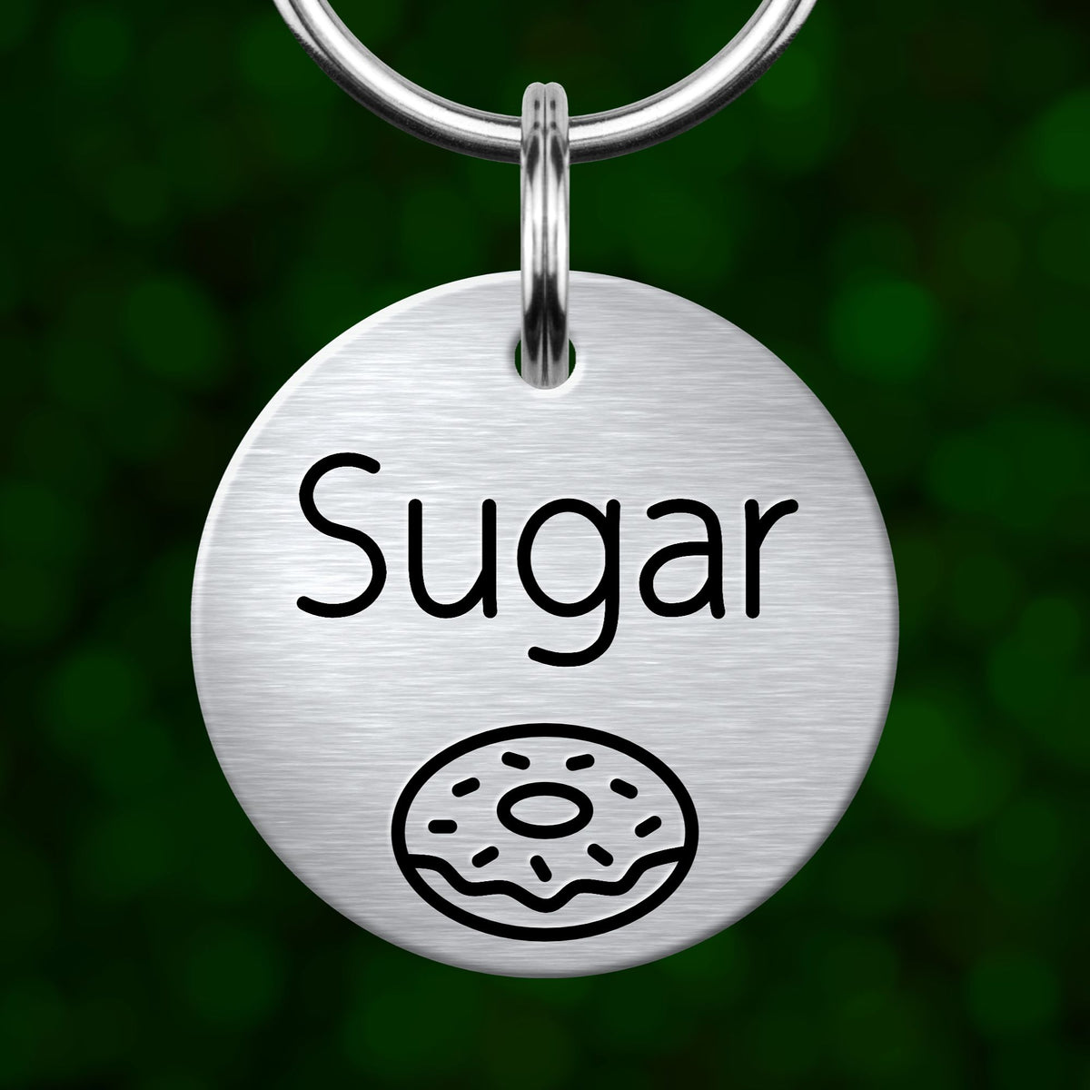 A round metal keychain tag with the word "Sugar" printed on it, along with a simple illustration of a donut.