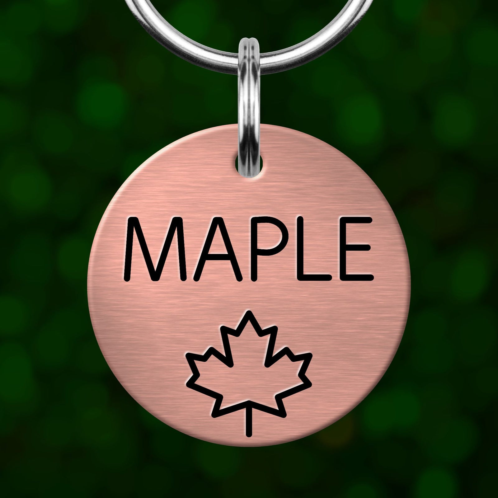 A round metal pet tag with the word "MAPLE" printed on it, along with a maple leaf symbol.
