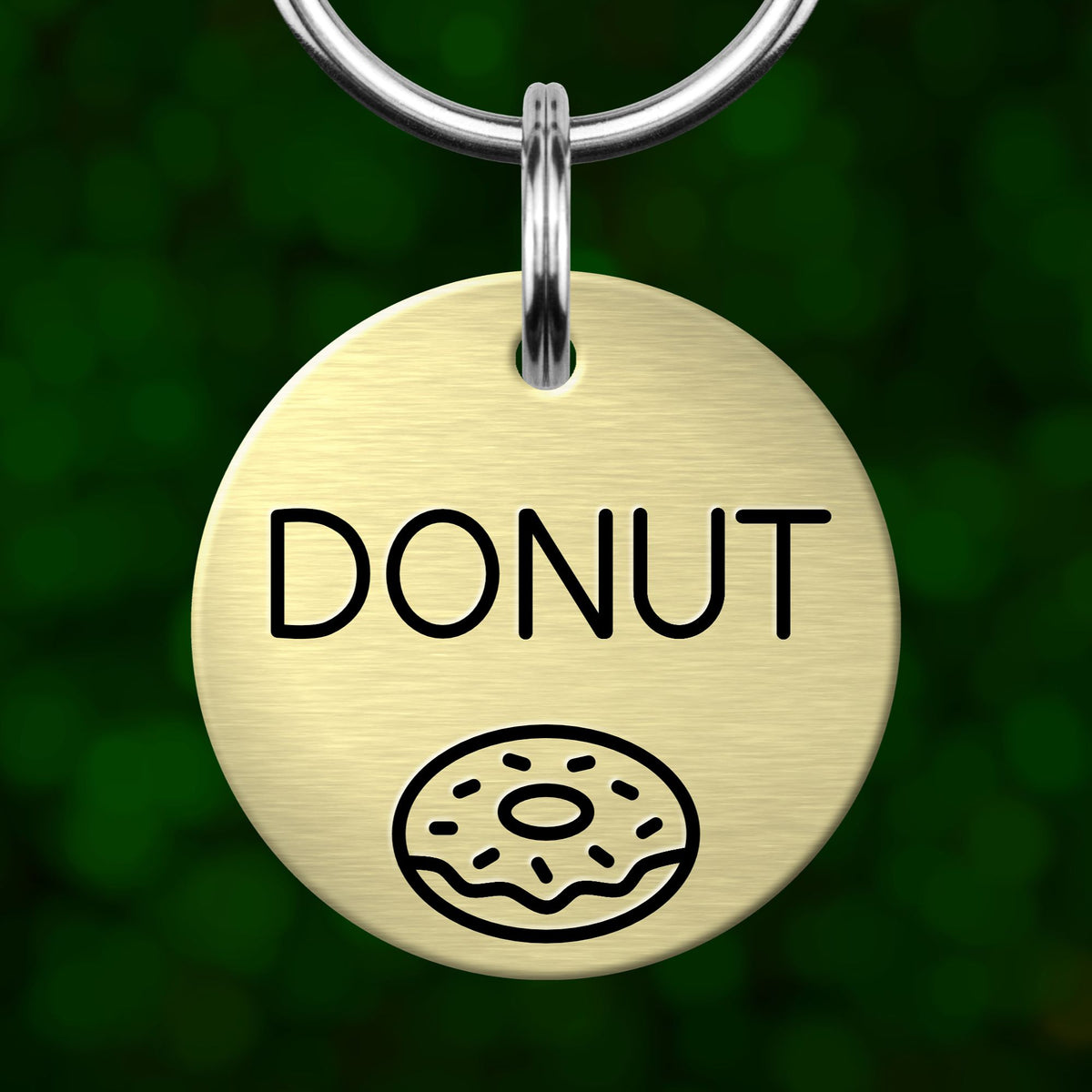 A round metal dog tag with the word "DONUT" printed on it, along with a simple illustration of a donut.
