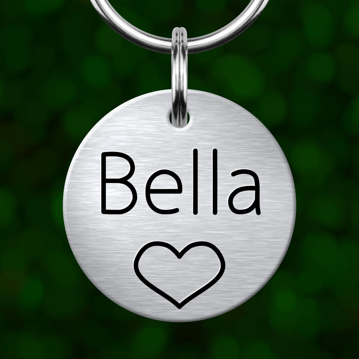 A round metal keychain tag with the name "Bella" and a heart symbol printed on it.