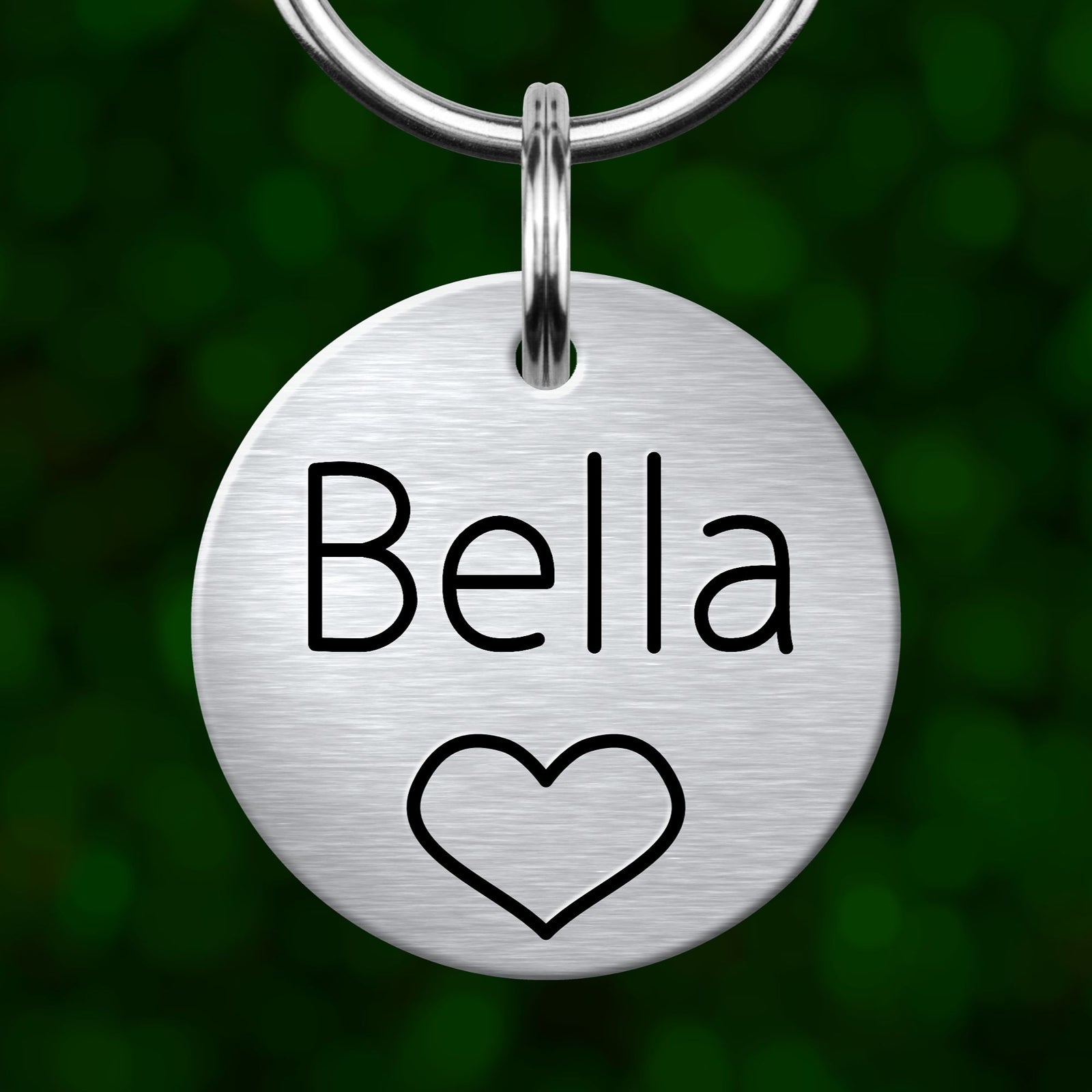 A round metal keychain tag with the name "Bella" and a heart symbol printed on it.