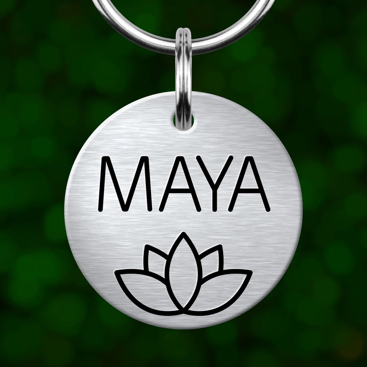 A silver metal keychain tag with the name "MAYA" printed on it, along with a simple black outline of a lotus flower.