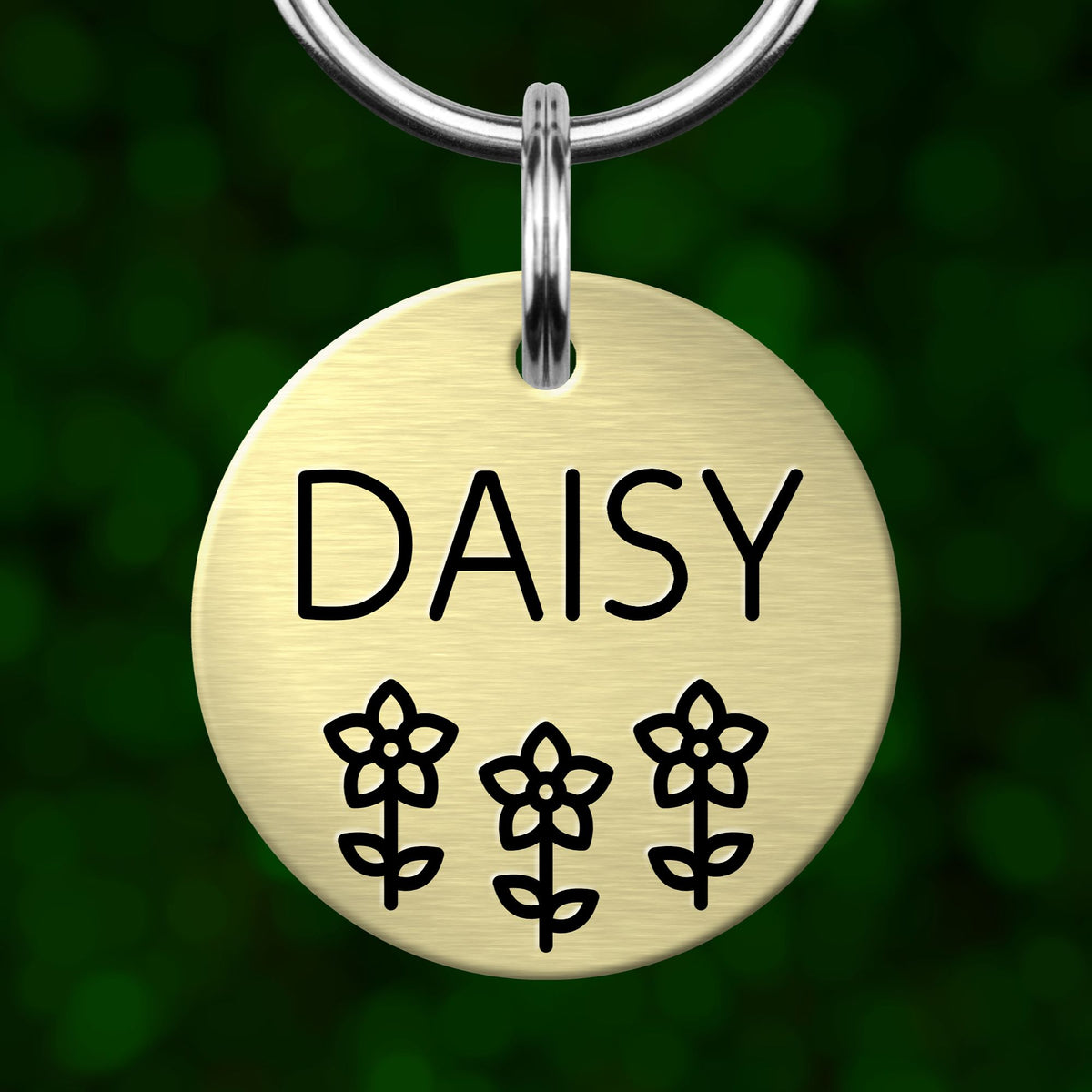 A round metal pet tag with the name "DAISY" and three flower icons printed on it.
