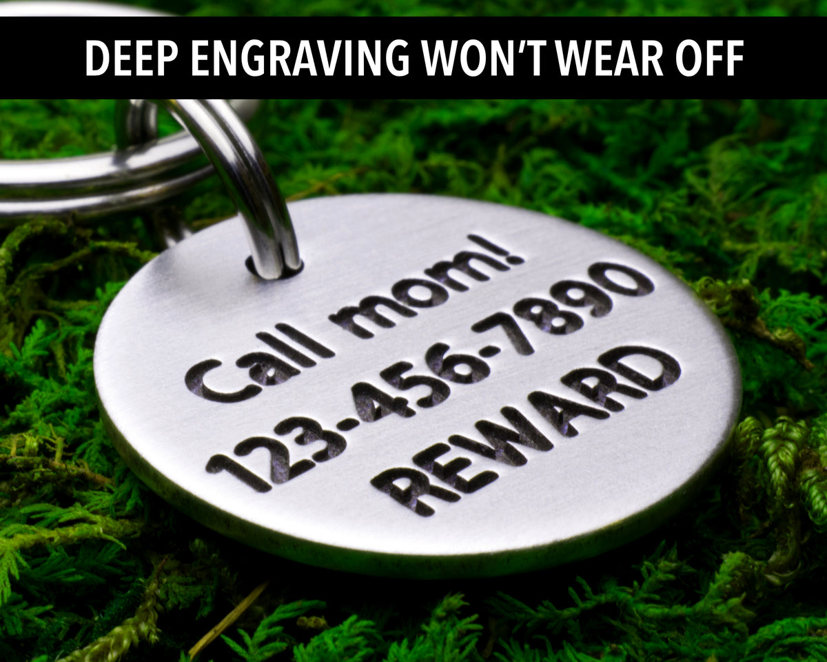 A metal keychain with a personalized engraved message on it, placed on a bed of green moss.