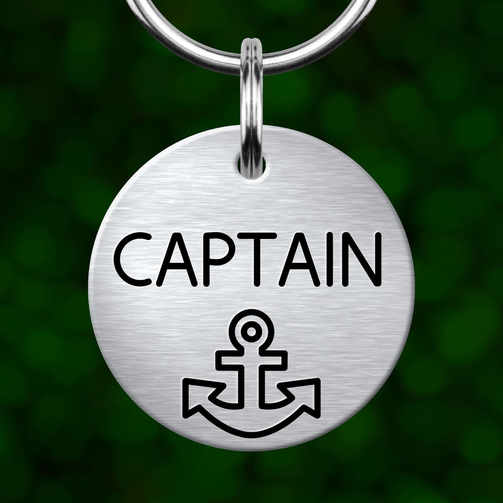 A round metal keychain tag with the word "CAPTAIN" printed on it, along with an anchor symbol.