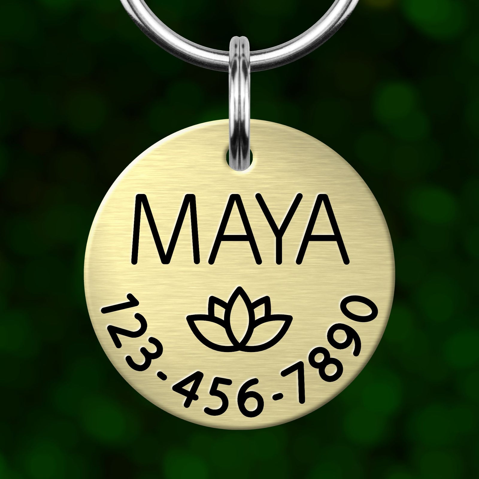 A round metal pet tag with the name "MAYA" printed on it, along with a phone number and a symbol.