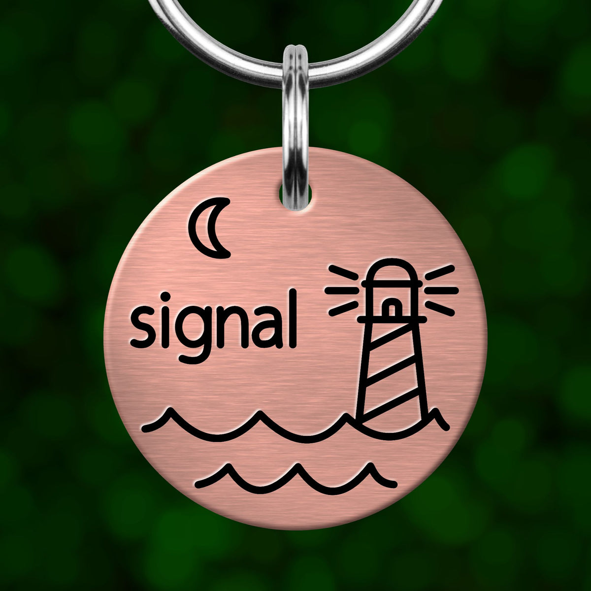 A round metal keychain tag with a lighthouse and waves design, and the word "signal" printed on it.