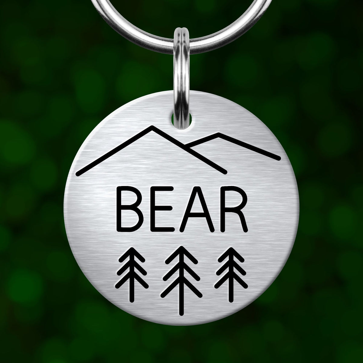 A silver metal keychain with a circular design featuring a mountain silhouette and the word "BEAR" below it.