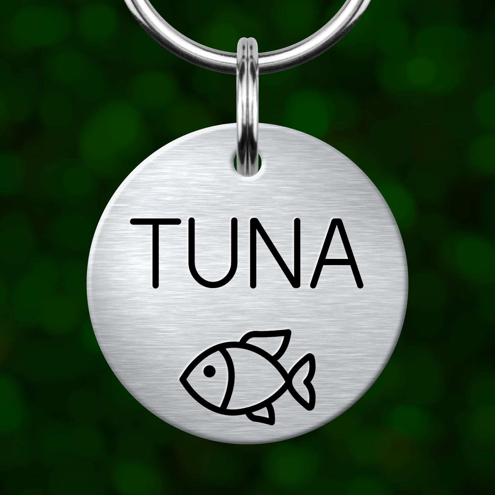 A round metal pet tag with the word "Tuna" printed on it, featuring a simple black and white illustration of a fish.