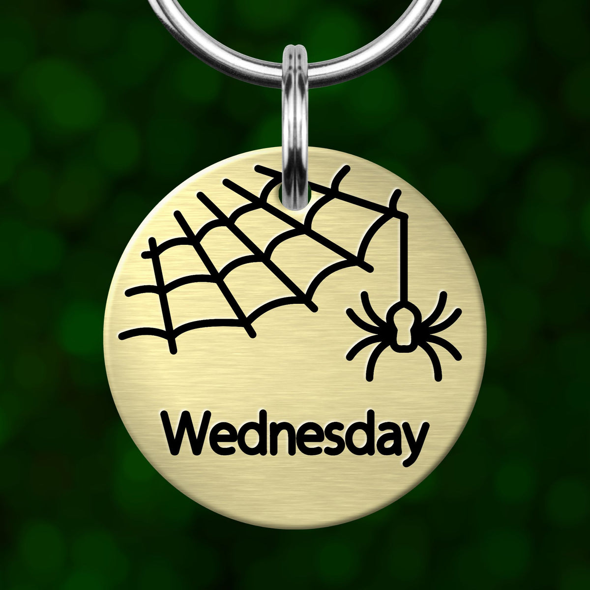 A round metal keychain tag with a spider and web design, and the word "Wednesday" printed on it.
