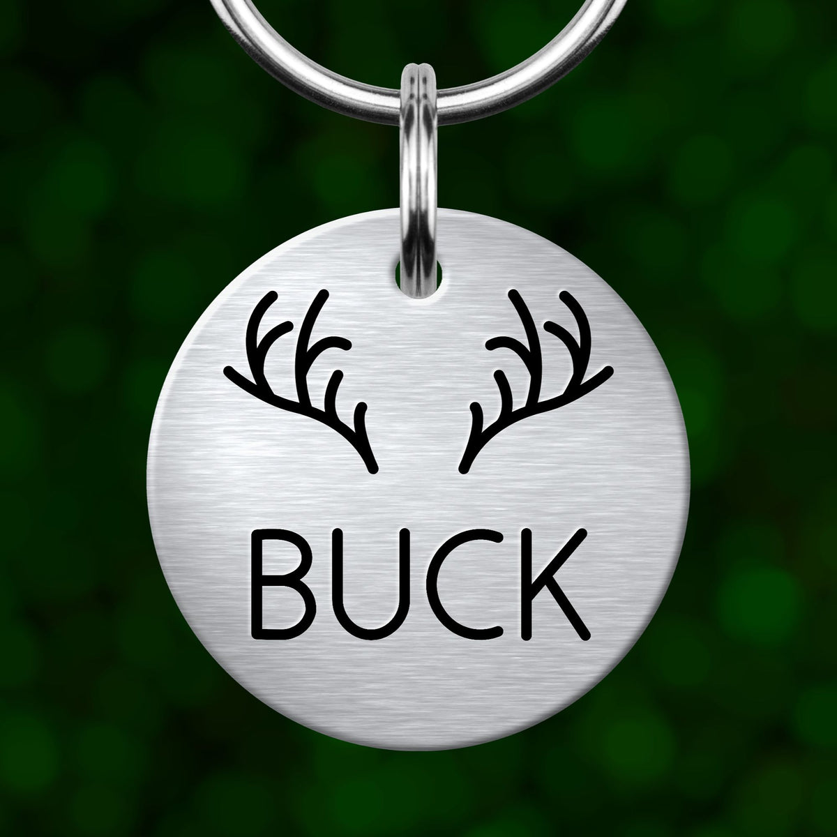 A silver metal keychain tag with the word "BUCK" printed on it, featuring a pair of antlers.