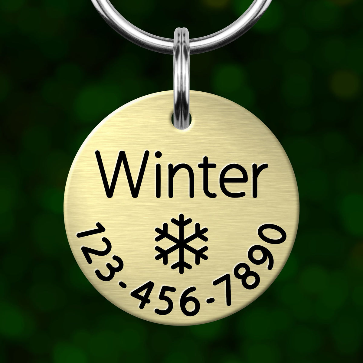 A round metal pet tag with the word "Winter" printed on it, along with a snowflake symbol and a phone number.