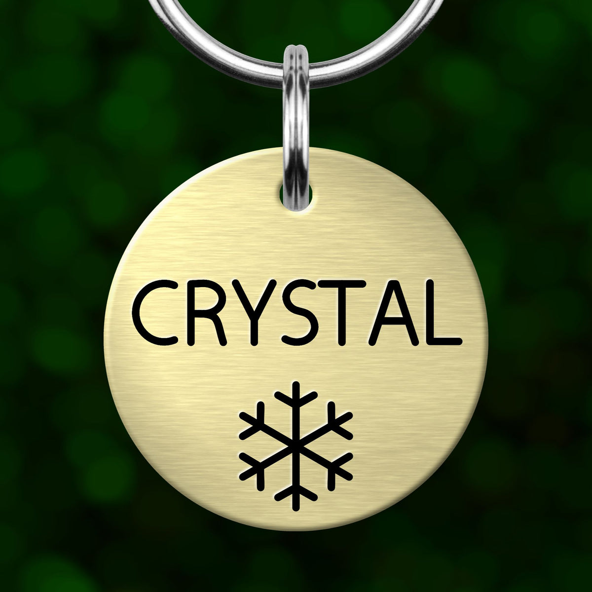 A round, gold-colored pet tag with the word "CRYSTAL" printed on it, along with a snowflake symbol.