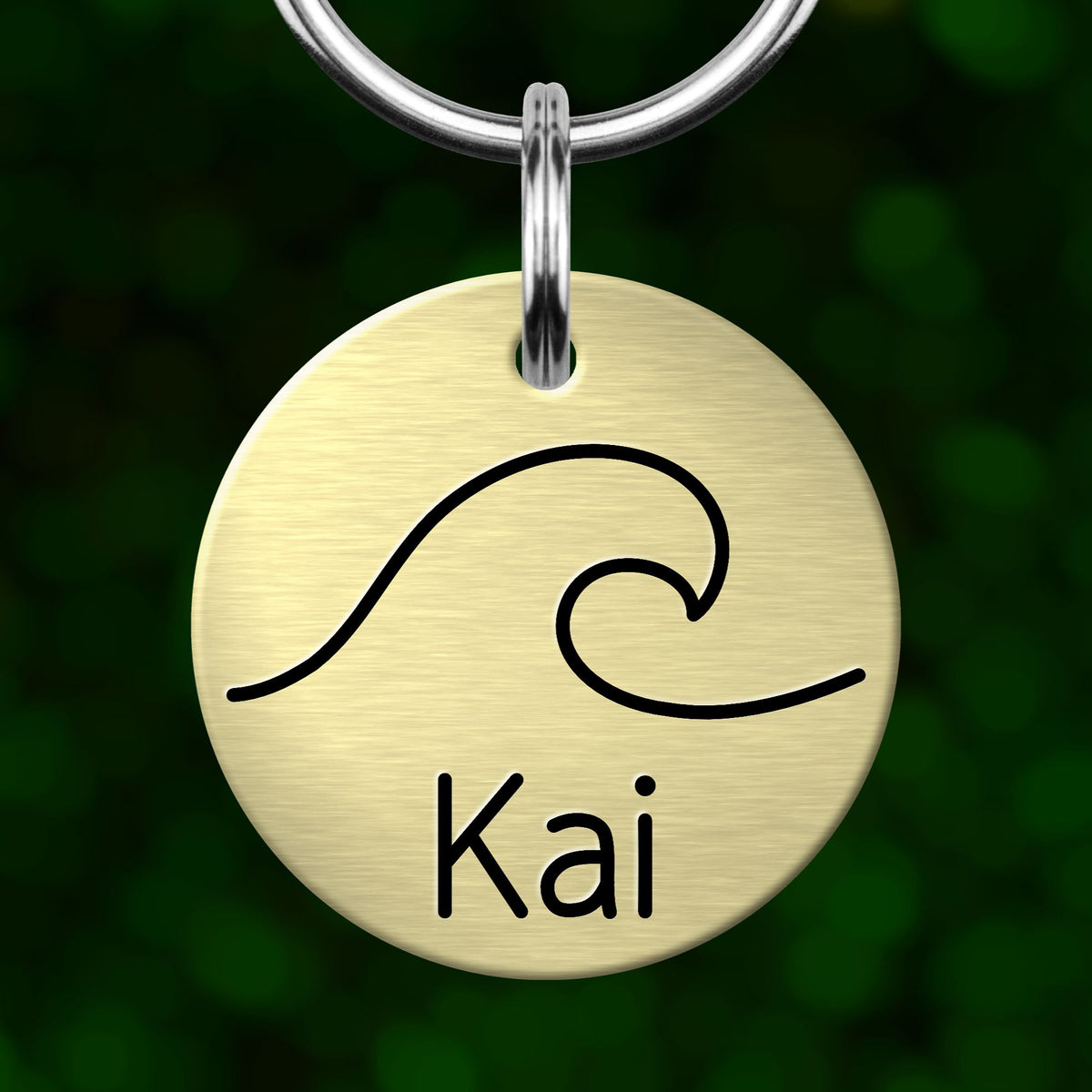 A round metal pet tag with a wave design and the name "Kai" printed on it.