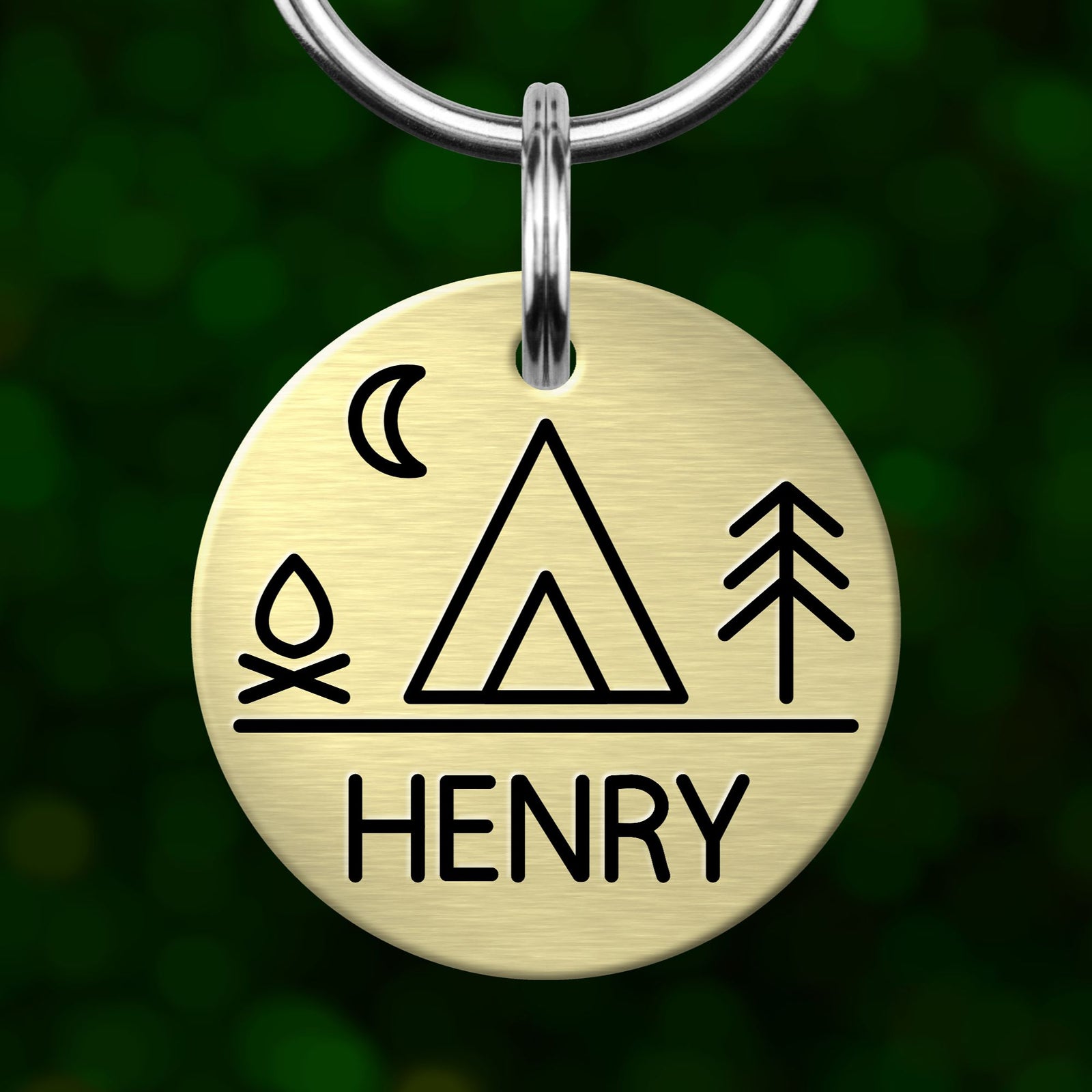 A round metal keychain tag with a camping-themed design, including a tent, a crescent moon, and a campfire symbol.