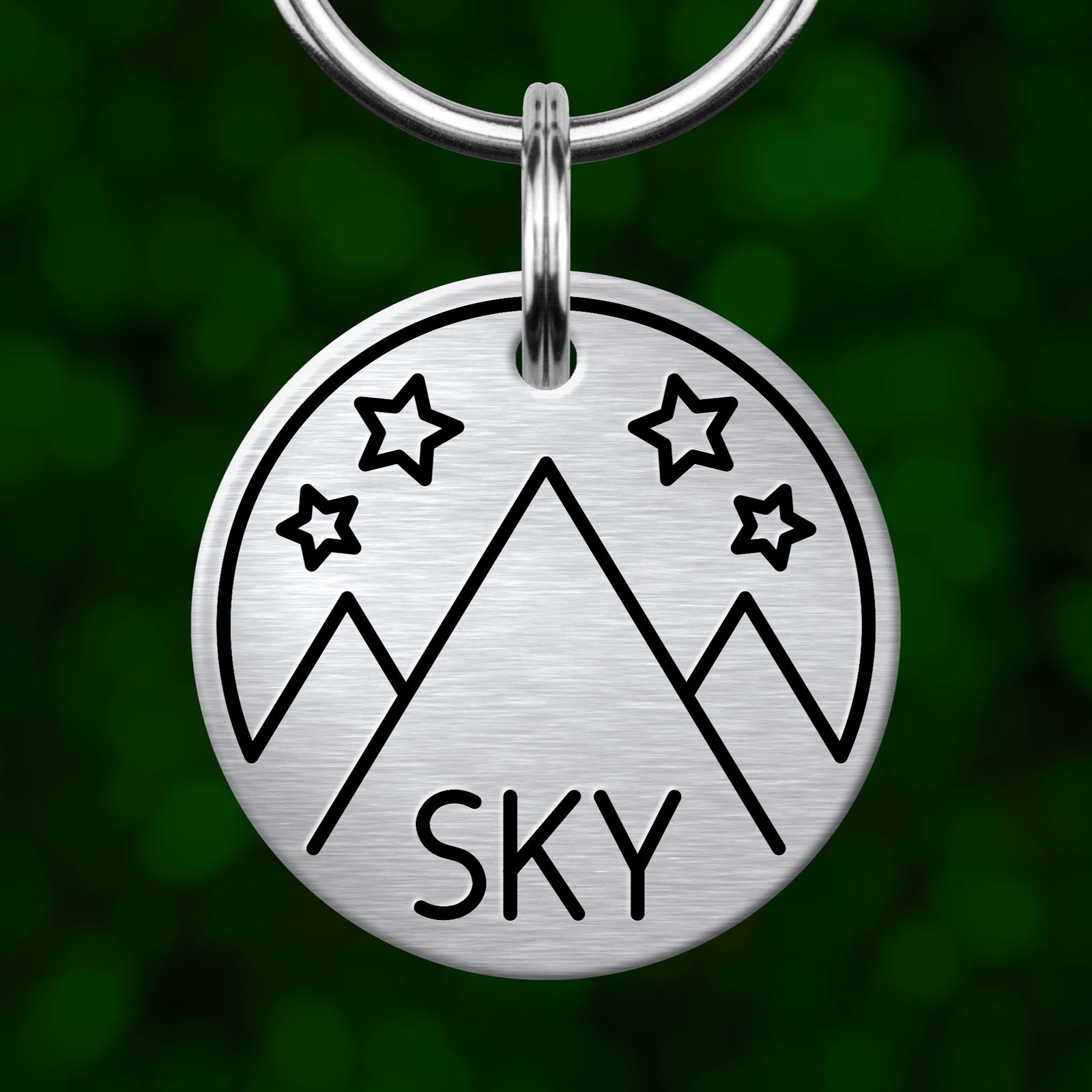 A silver-colored keychain with a circular design featuring mountains and stars.