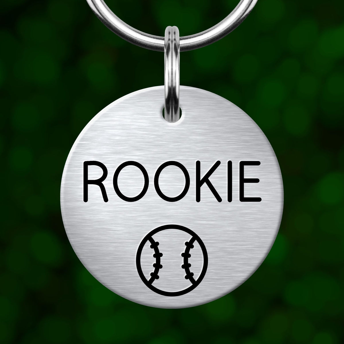 A round metal keychain tag with the word "ROOKIE" printed on it, along with a baseball symbol.