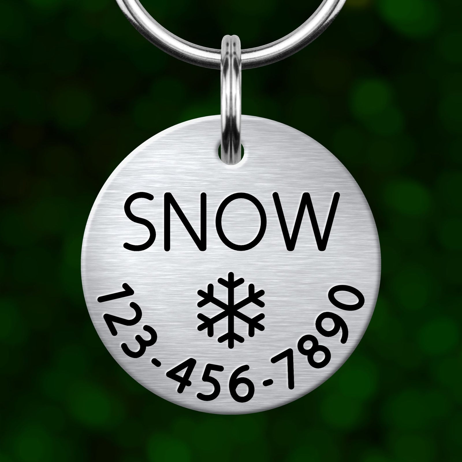 A silver metal tag with the word "SNOW" printed on it, along with a snowflake symbol and a phone number.