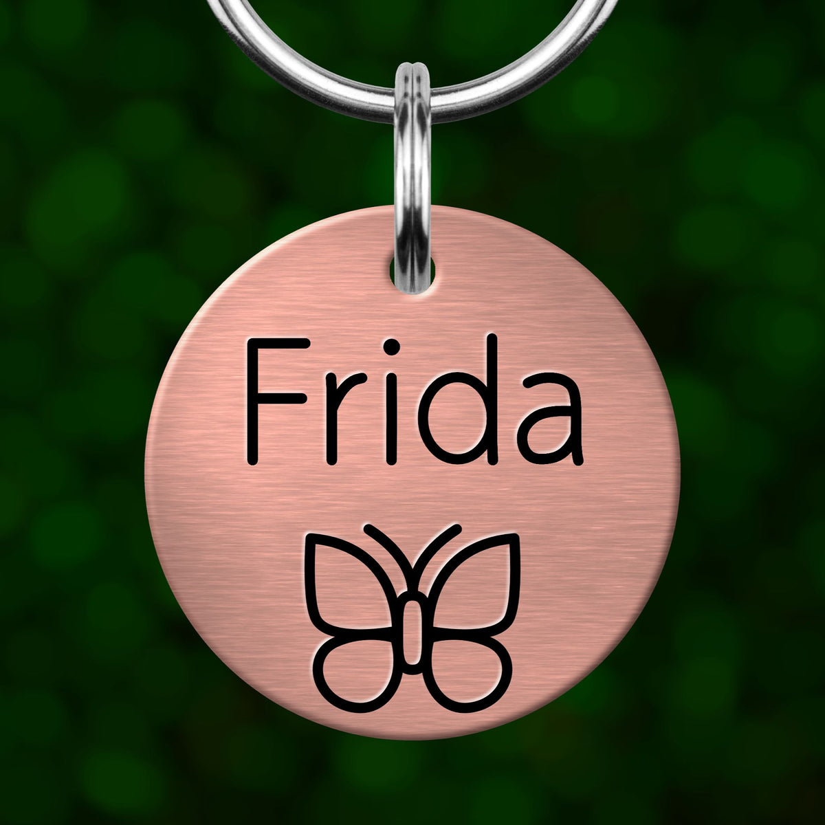 A round metal pet tag with the name "Frida" and a butterfly symbol printed on it.