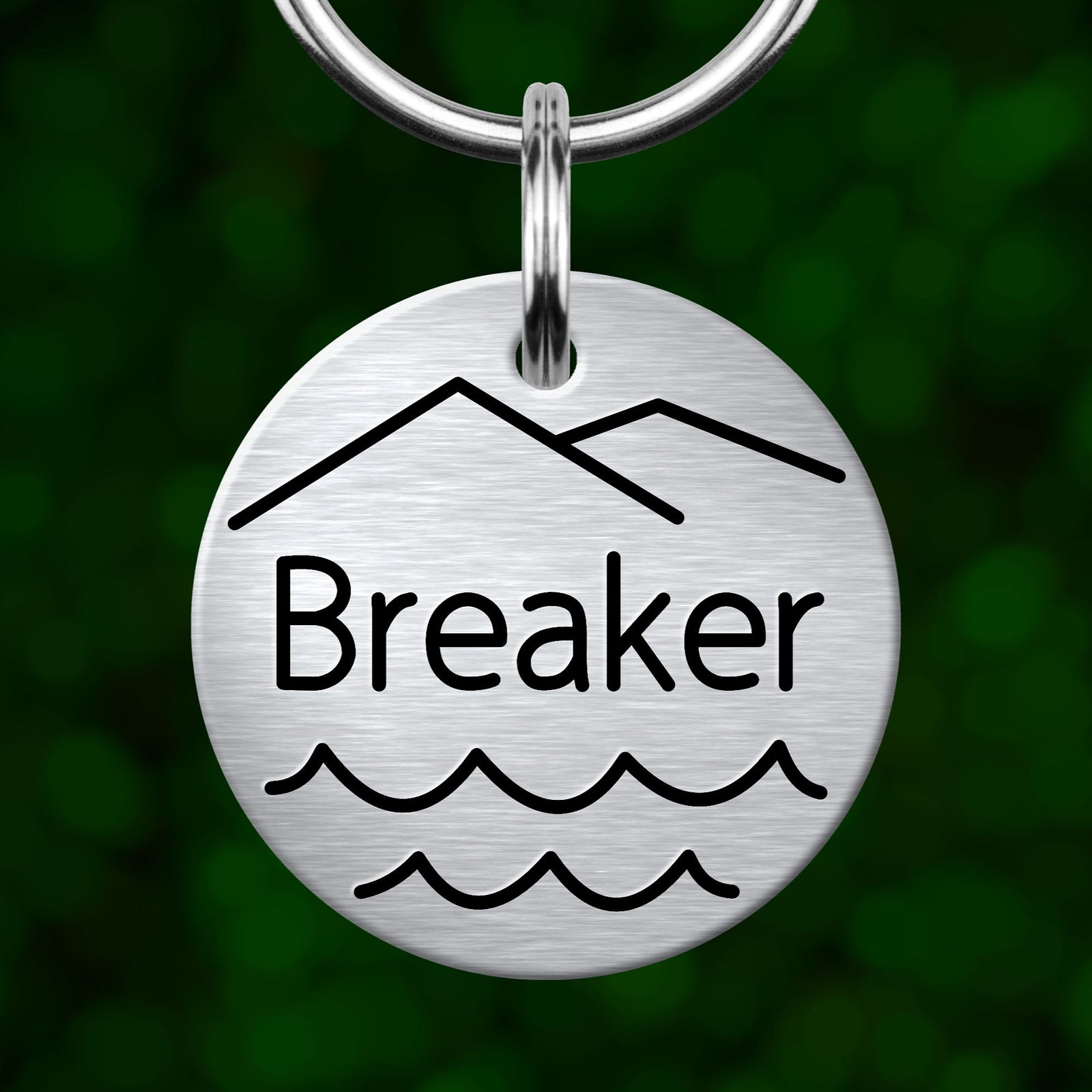 A round metal keychain tag with the word "Breaker" printed on it, featuring a mountain silhouette and wavy lines.