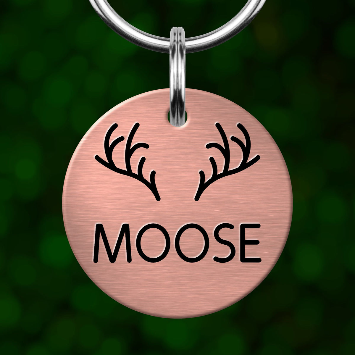 A round metal keychain tag with the word "MOOSE" printed on it, featuring a pair of antlers.