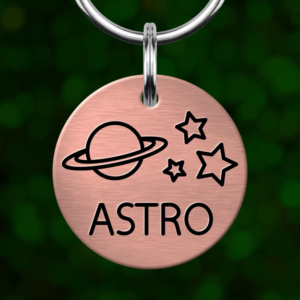A circular metal keychain with a pink background and black text and graphics, including a planet, stars, and the word "ASTRO".