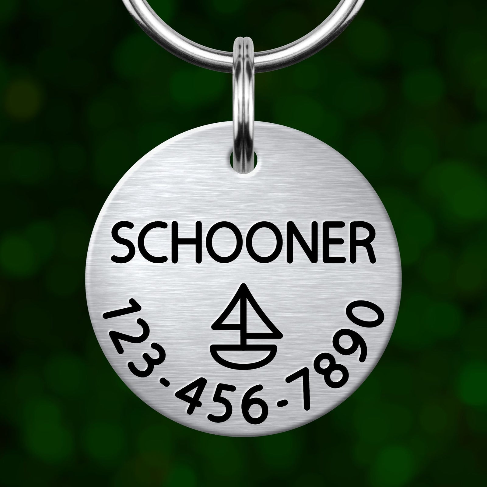 A silver-colored metal keychain tag with the name "SCHOONER" printed on it, along with a phone number and a symbol resembling a boat.
