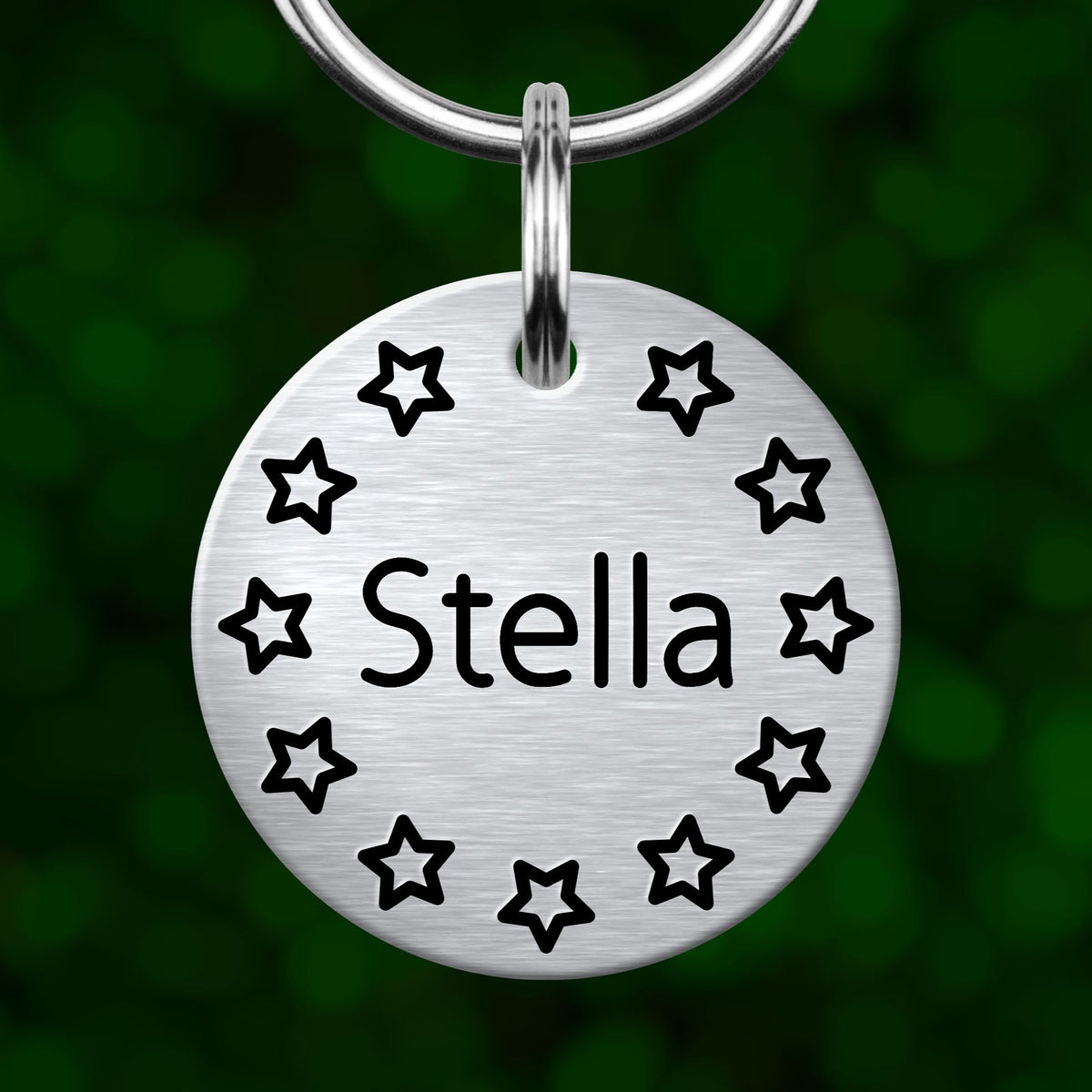 A silver circular tag with the name "Stella" and a star pattern around it, hanging from a keychain.