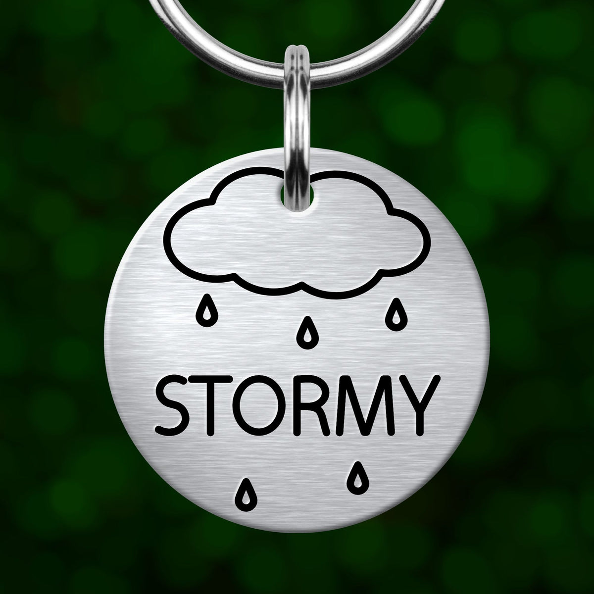 A round metal keychain tag with a cloud and rain symbol, and the word "STORMY" printed on it.