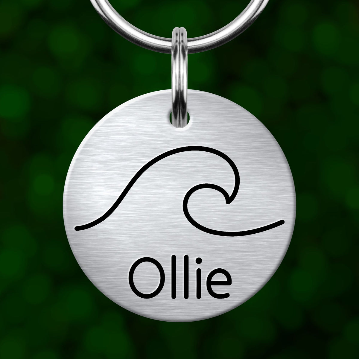 A silver circular pet tag with a wave design and the name "Ollie" printed on it.